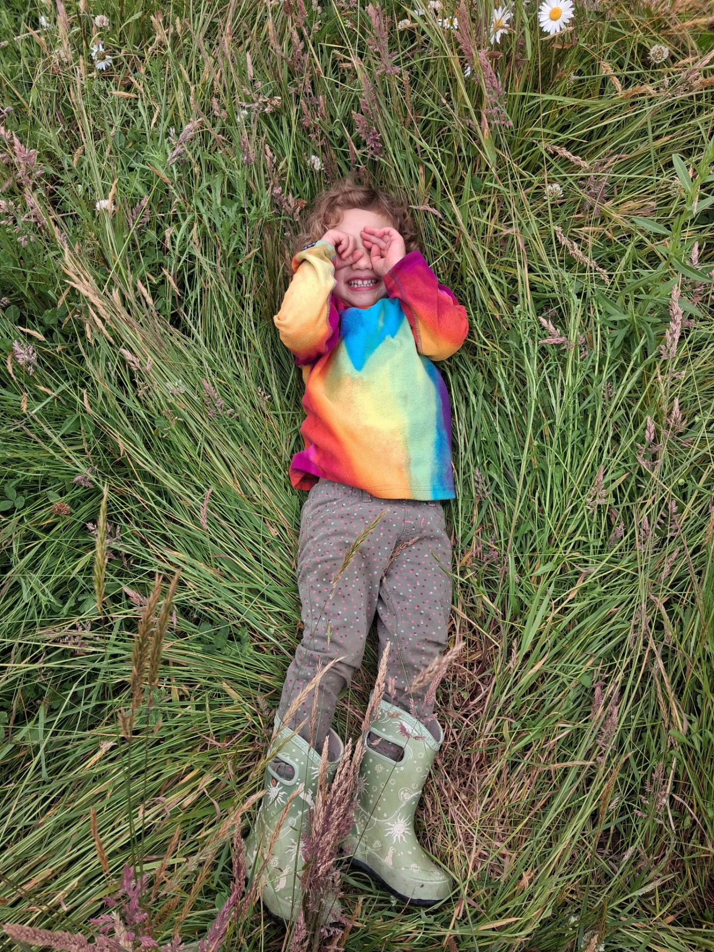 Child lying in tall meadow grass at our outdoor school in McKinleyville, CA